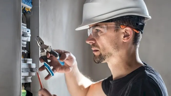 Elektriker med hjelm og vernebriller arbeider i et sikringsskap