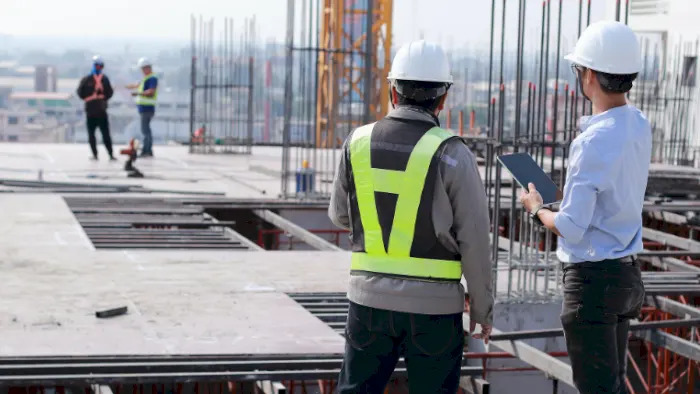 To personer med hjelm som går gjennom en byggeplass